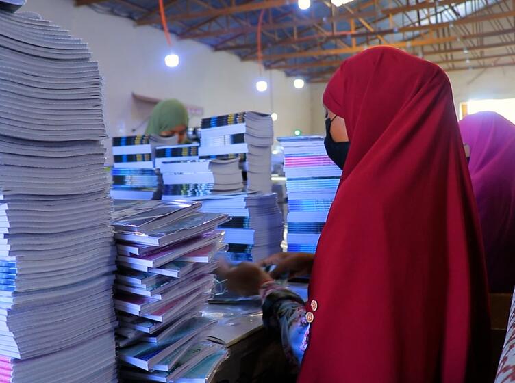 Women at AADCO paper factory wrapping booklets at a table surrounded by many booklets