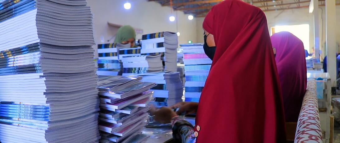 Women at AADCO paper factory wrapping booklets at a table surrounded by many booklets