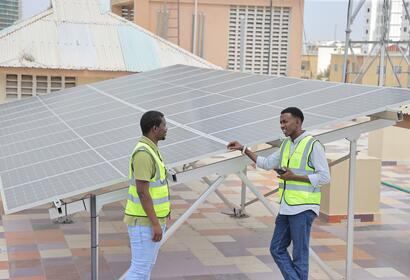 2 SolarGen employees standing next to a solar panel on a rooftop smiling