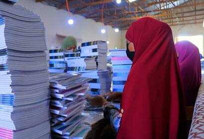 Women at AADCO paper factory wrapping booklets at a table surrounded by many booklets